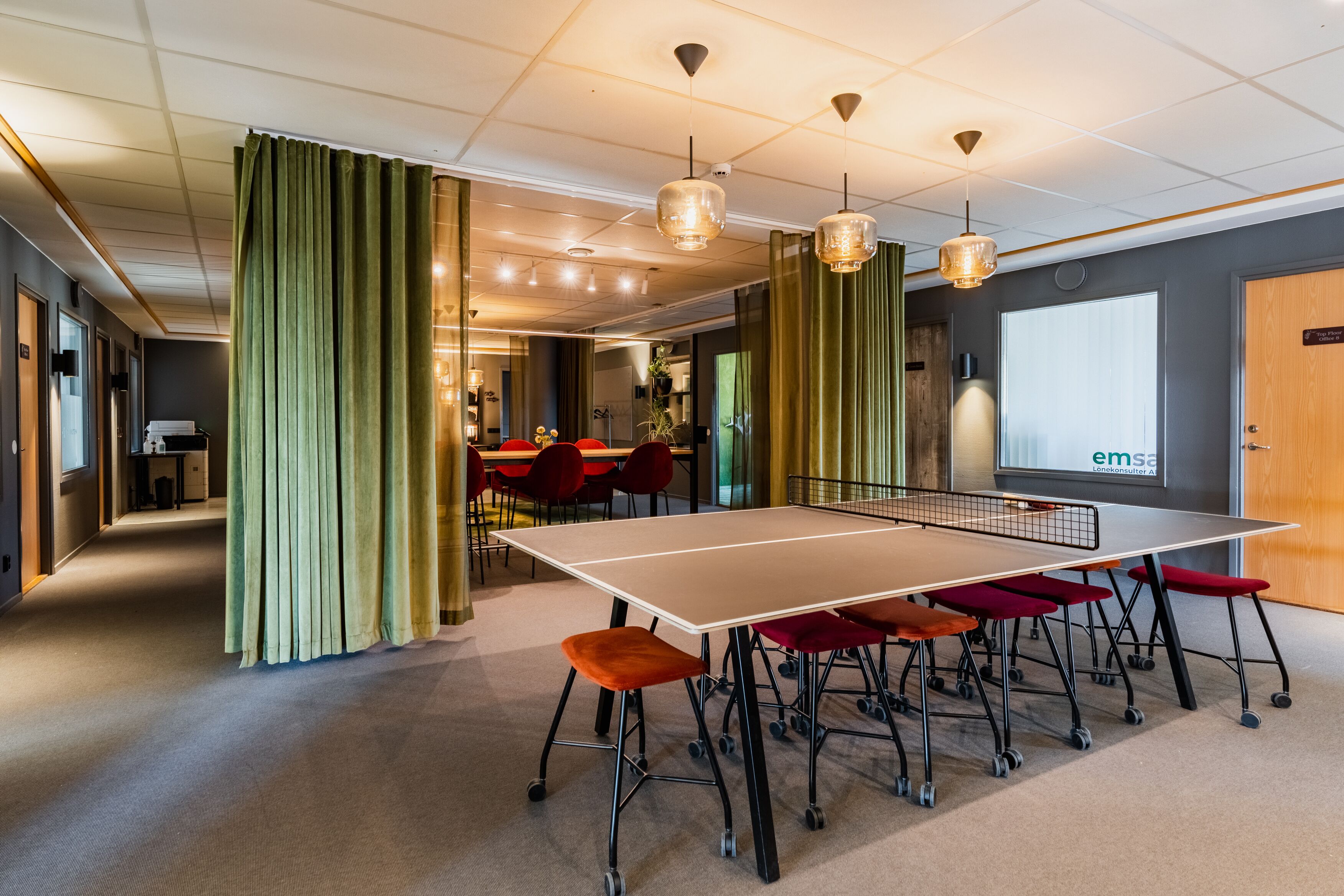 A conference room with a large table, red chairs, and green curtains.