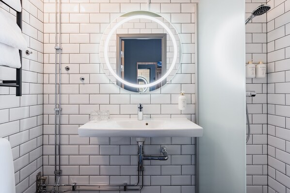 A bathroom with white tiled walls, a white sink with a mirror, and a shower area.