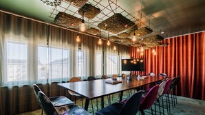 A conference room with a long table, chairs, a television, and a red curtain backdrop. - Hotell Fridhemsgatan (Mora)