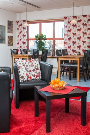 A modern living room with a red carpet, black leather sofa, and a dining area with wooden tables and chairs.