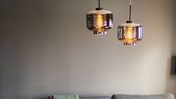 A modern living room with a grey sofa, a white armchair, a round coffee table with wine glasses, and two hanging pendant lights.