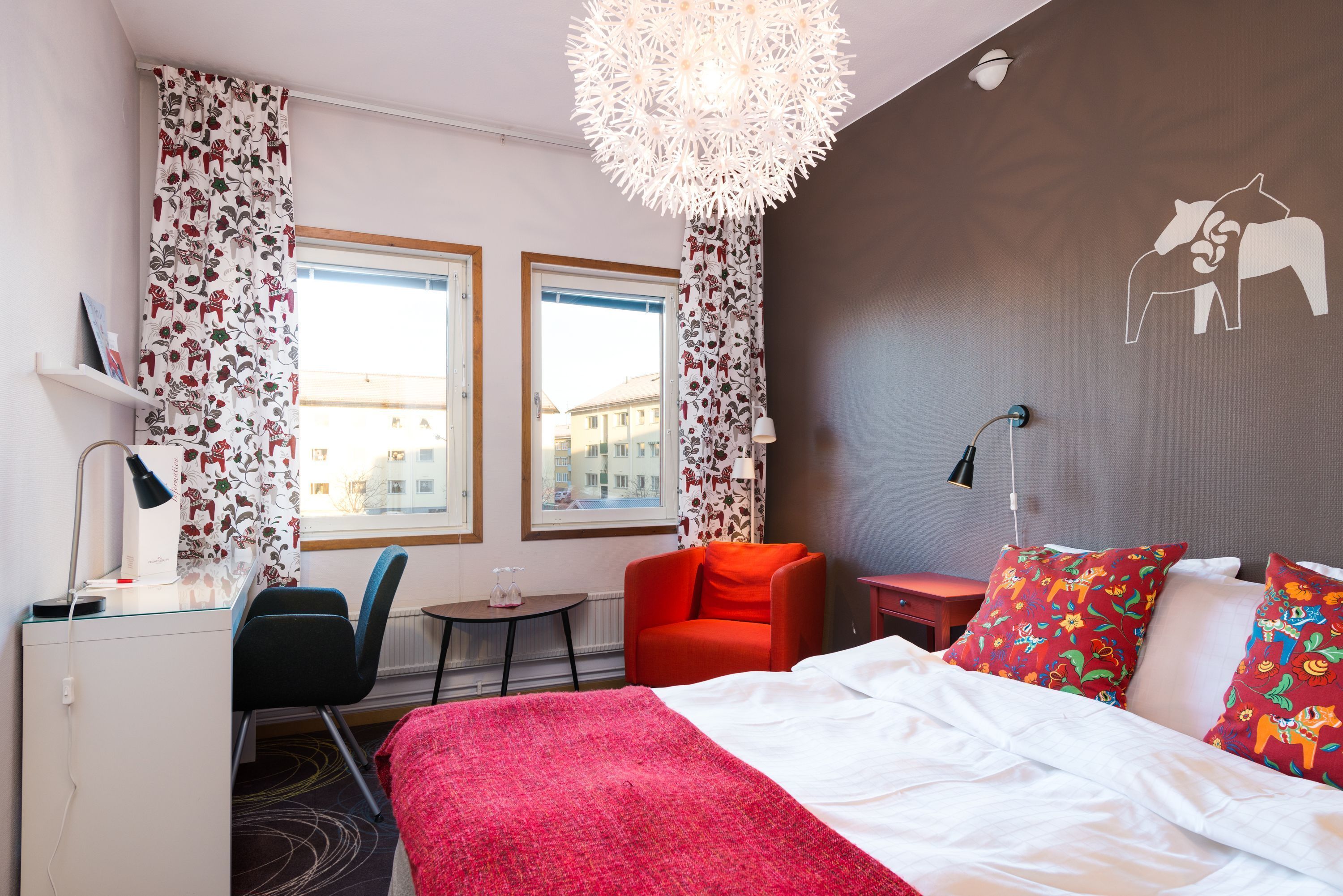 A hotel room with a bed, a desk, a chair, a small table, and a window.