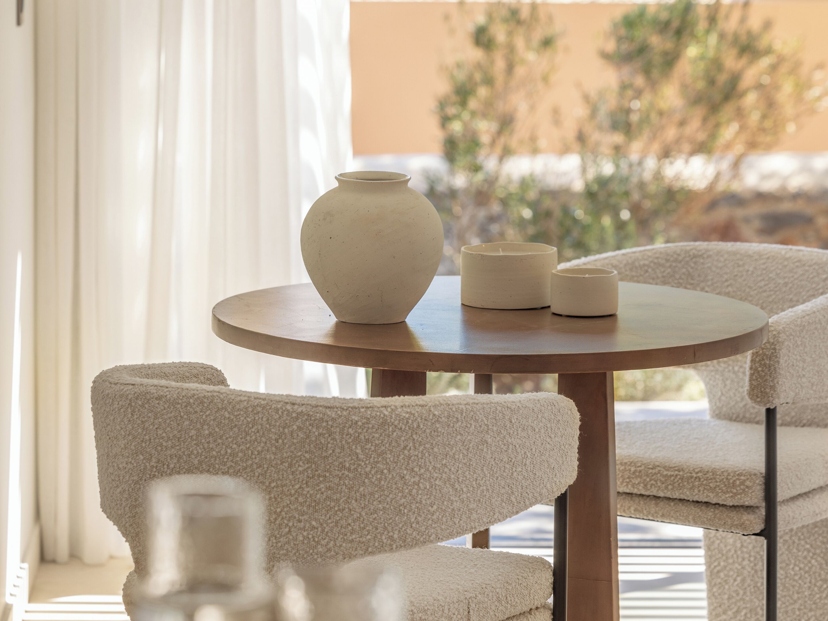 A round wooden table with a beige vase and two candles. There are beige chairs around the table.
