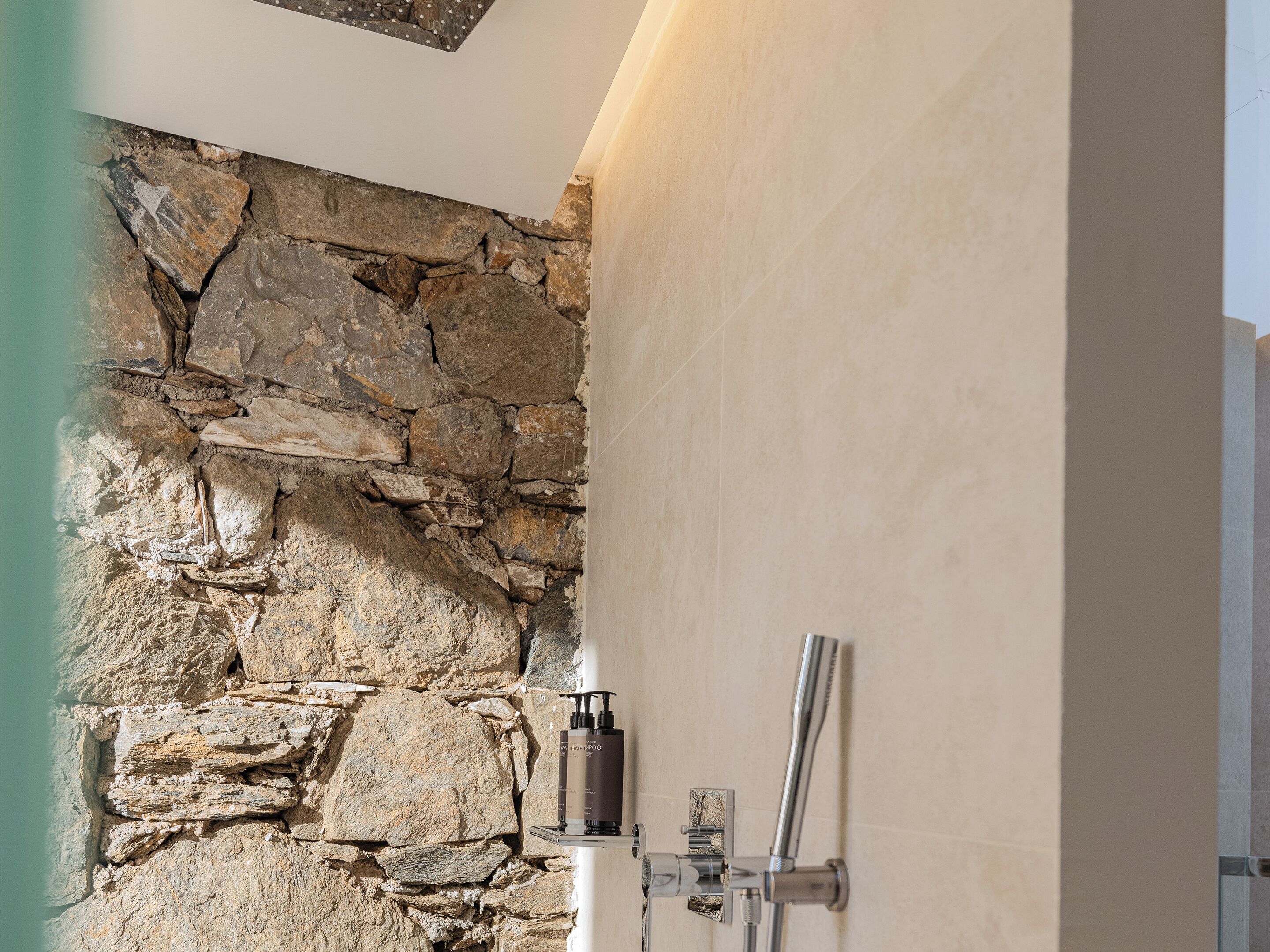 A bathroom with a stone wall and a modern shower.