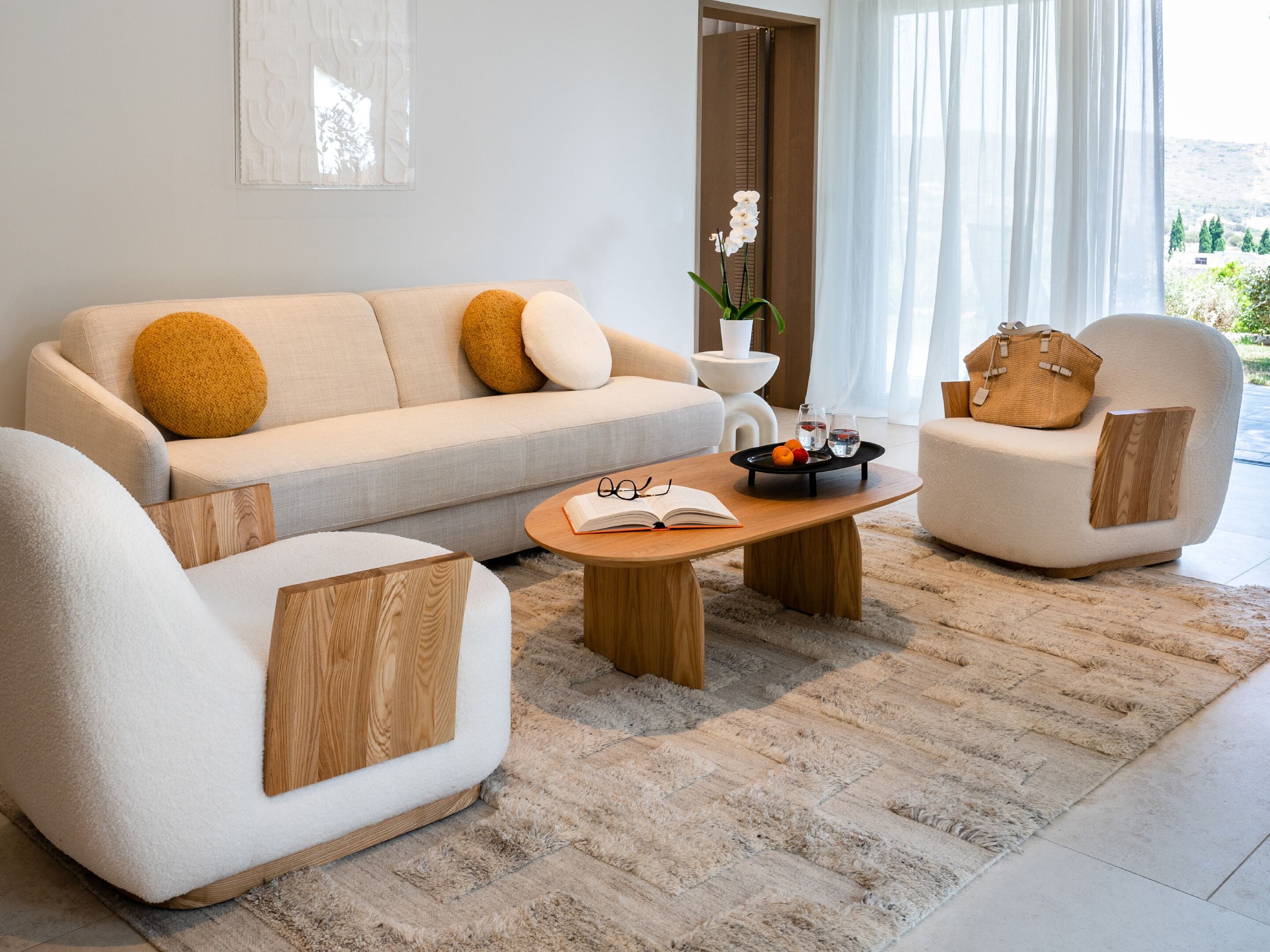 Un salon moderne avec un canapé, deux fauteuils, une table basse et une vue sur l’extérieur.
