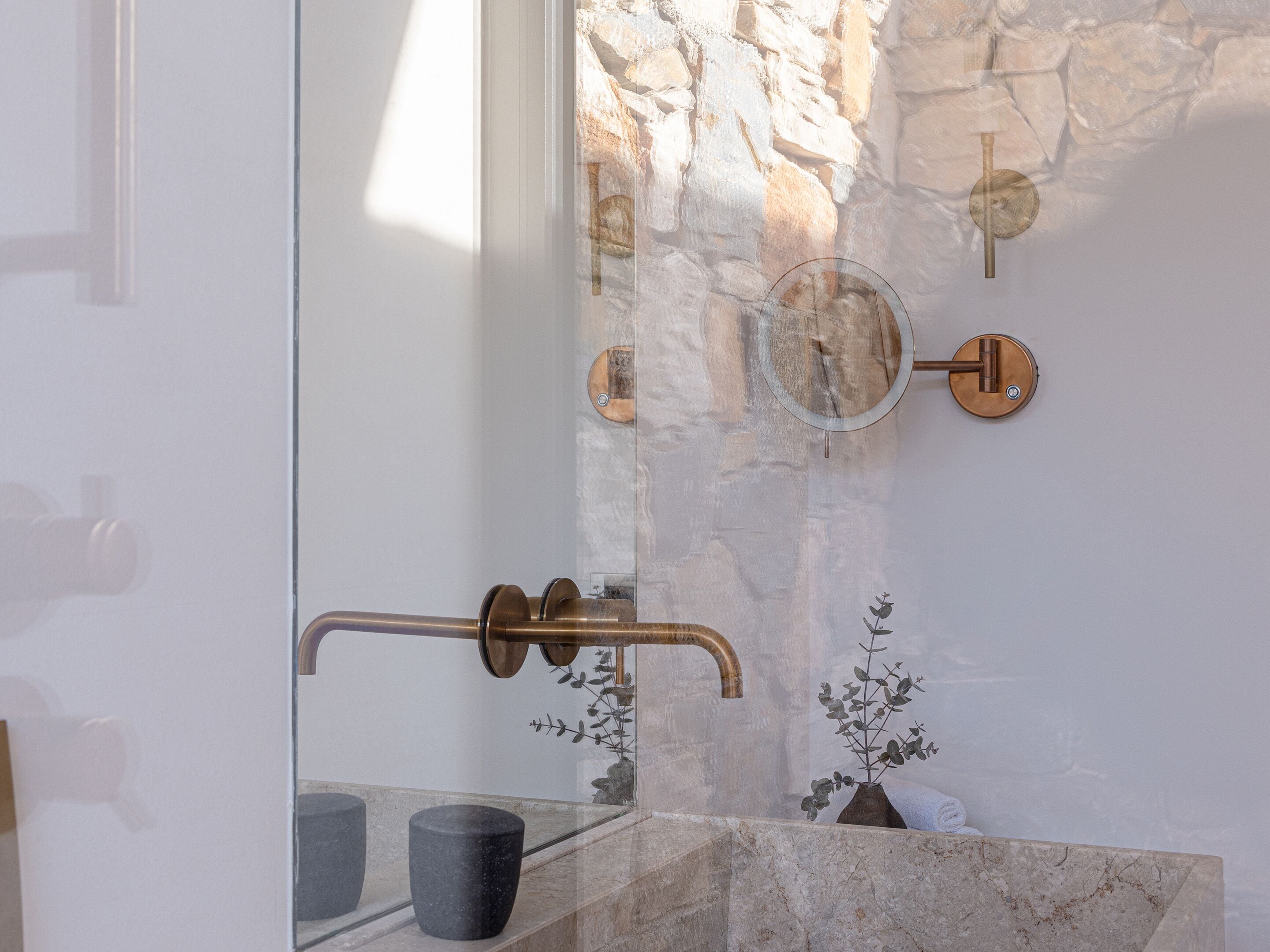 A modern bathroom with a stone wall, a glass shower enclosure, and a marble sink.
