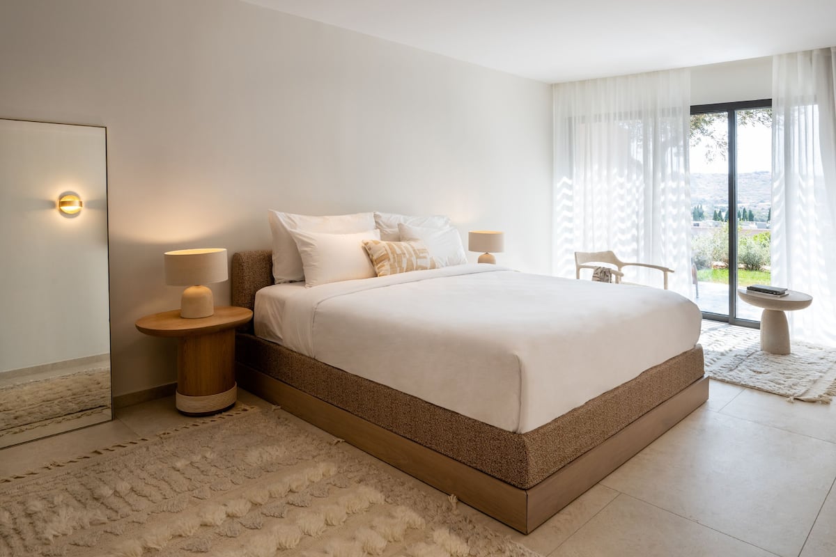 Ein Schlafzimmer mit einem großen Bett, zwei Nachttischen, einem Spiegel und Blick ins Freie.
