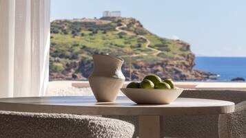 Una mesa con un cuenco de limones y un florero, con vista a un paisaje costero con un acantilado y un faro.