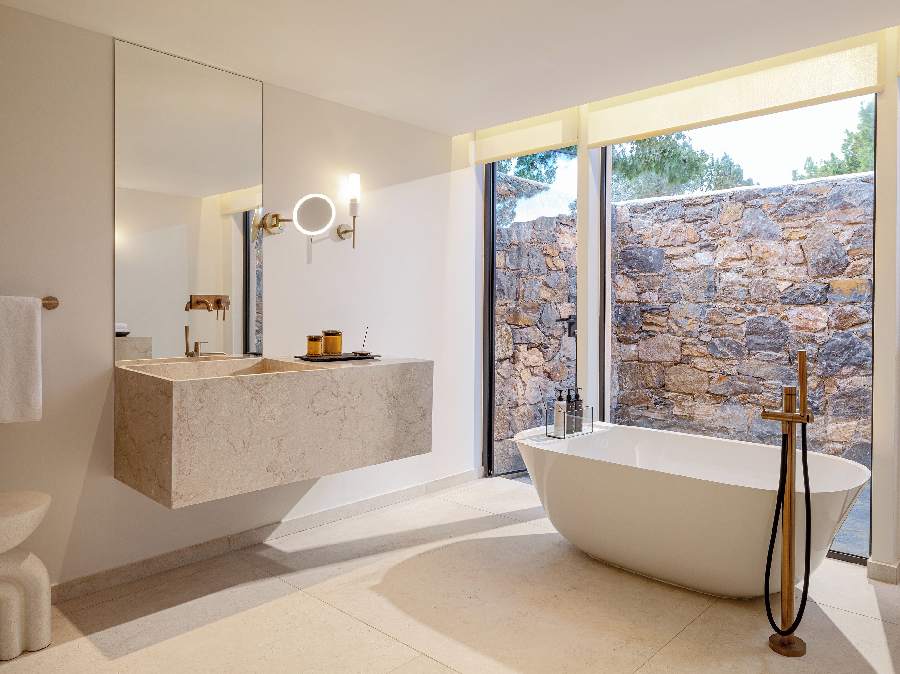 Une salle de bain moderne avec une baignoire sur pieds, un meuble-lavabo en marbre et un mur en pierre en arrière-plan.