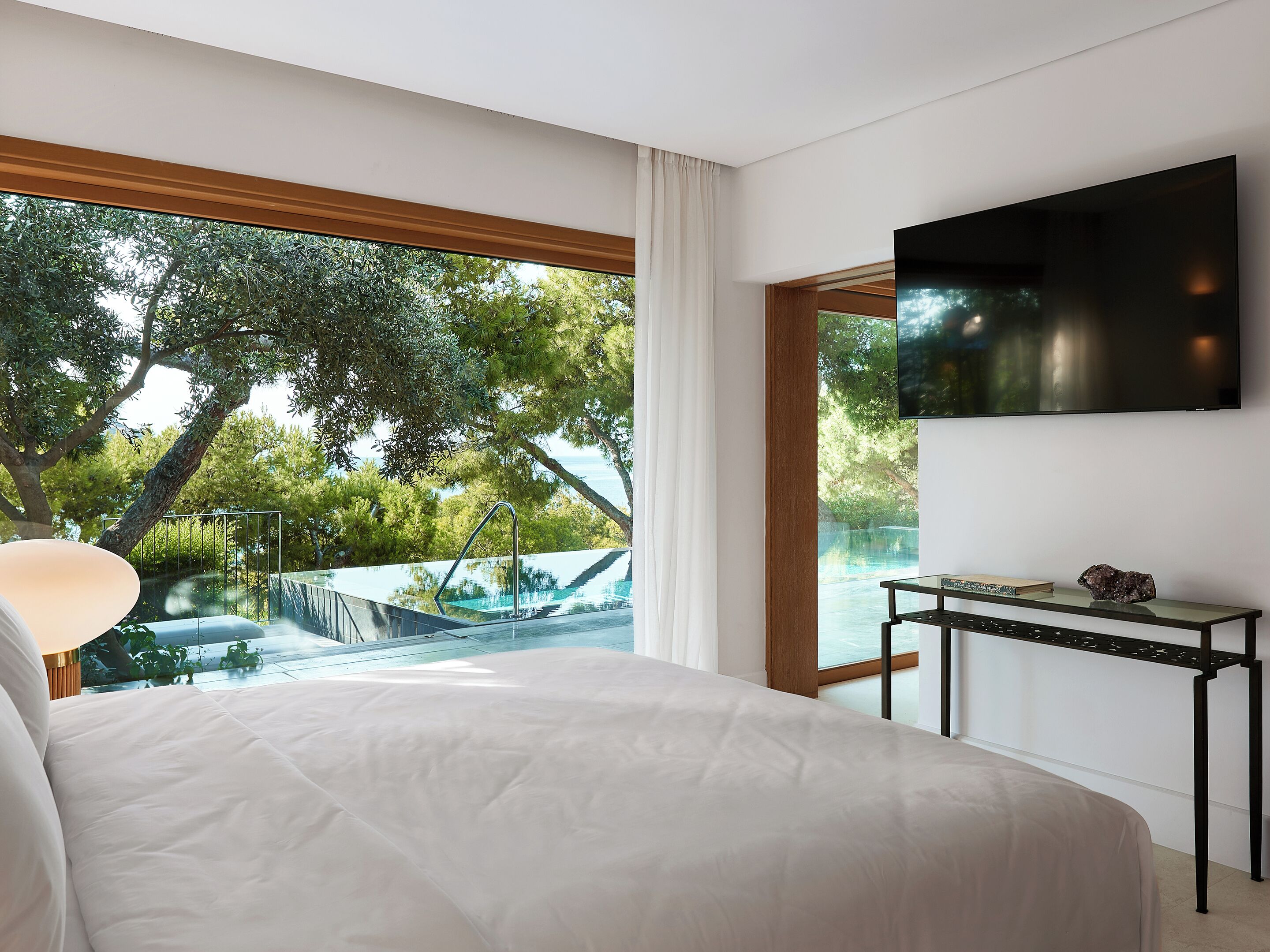 A bedroom with a large bed, a TV mounted on the wall, and a view of an outdoor swimming pool.