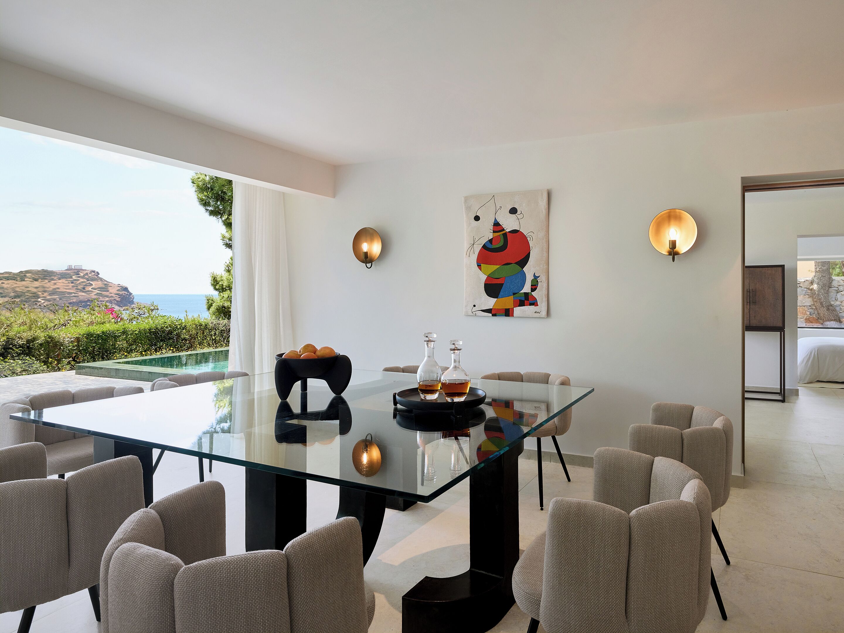 Een moderne eetruimte met een glazen tafel, beige stoelen en uitzicht op de oceaan.