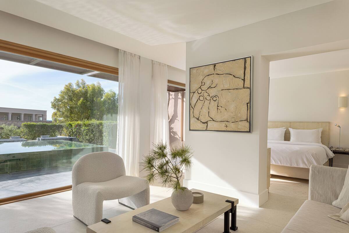 Ein modernes Hotelzimmer mit großem Fenster, einem Bett, einer Sitzecke mit Tisch und Blick auf ein Außenbecken.