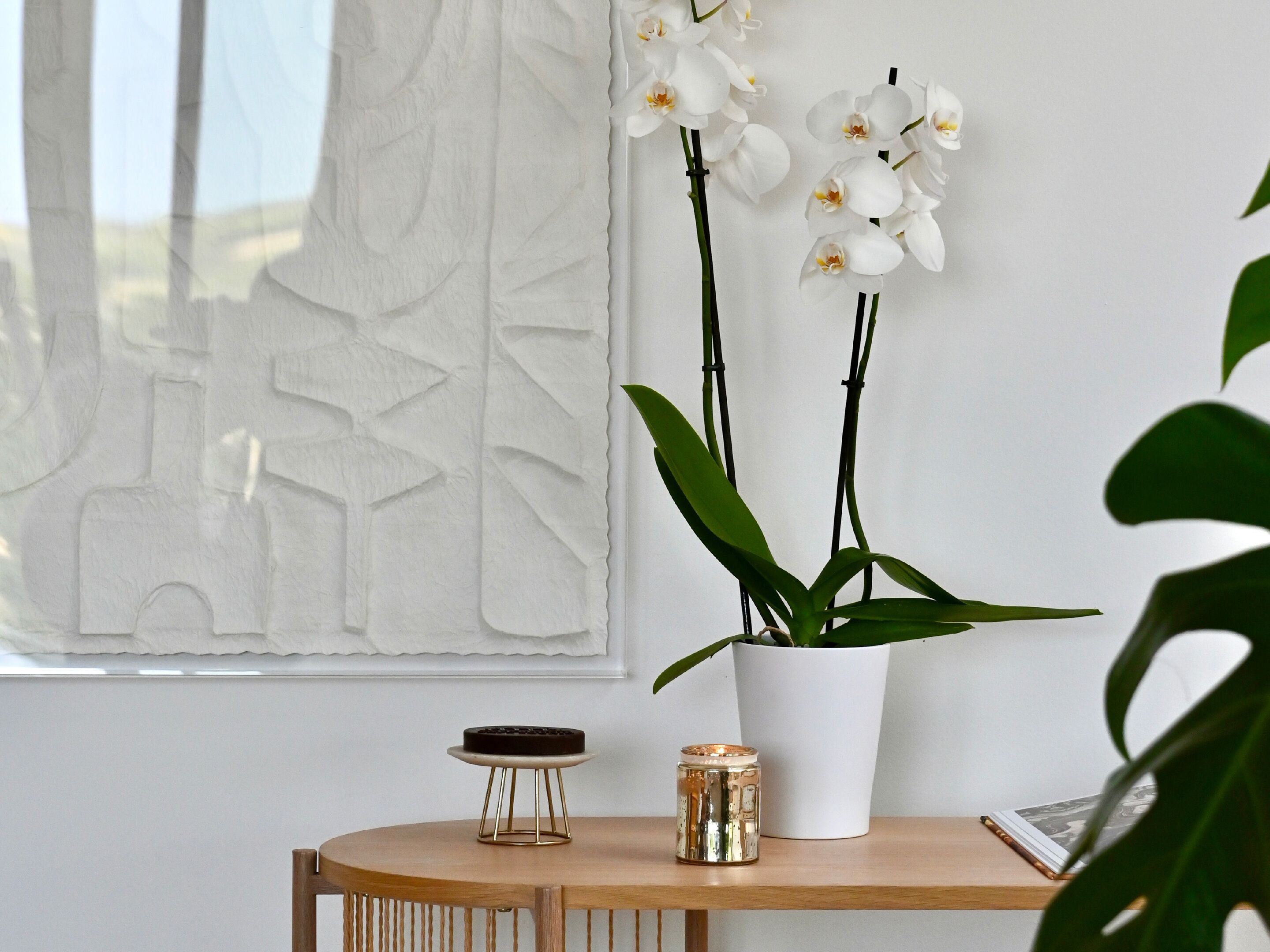 Une table en bois sur laquelle se trouve un vase blanc contenant des orchidées blanches, un petit bocal en verre et un livre.