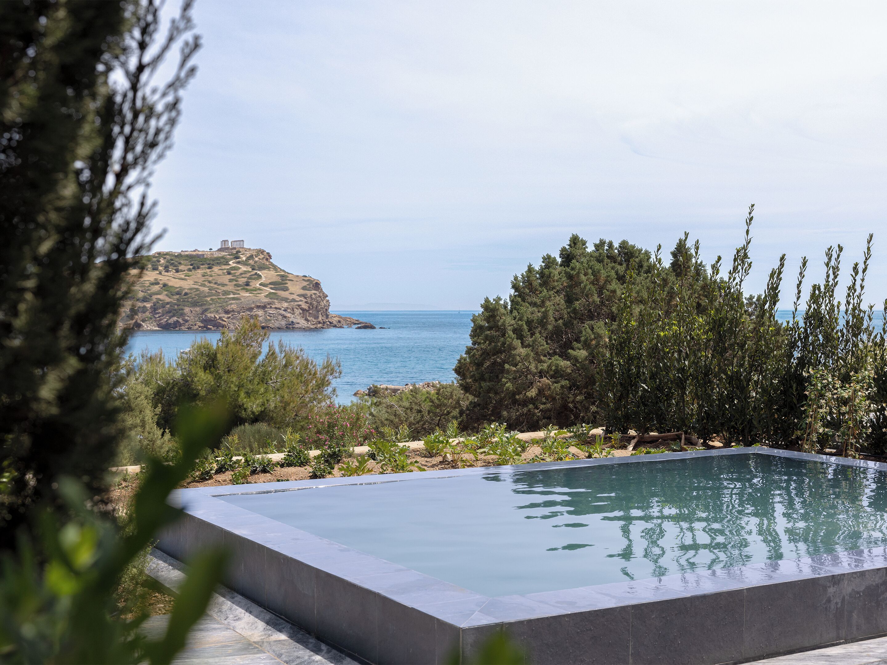 A swimming pool with a view of the sea and a rocky hill.