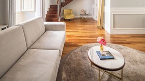Un salón espacioso con una escalera de madera, un sofá color beige, una mesa de centro redonda y un sillón amarillo.