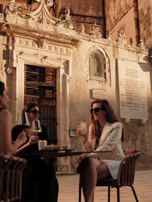 An outdoor seating area with ornate architectural details, a plaque commemorating an individual, and a table with drinks. -  Palazzo Artemide - VRetreats, SLH Collection (Syracuse)