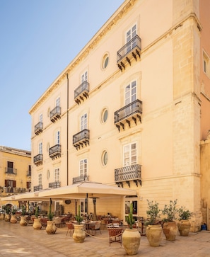 Un edificio de varios pisos con balcones, mesas al aire libre y plantas en macetas.