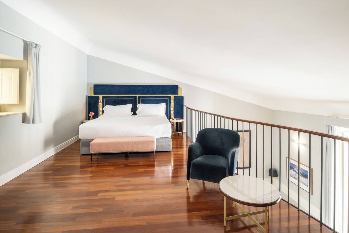 Une chambre à coucher avec un grand lit, une chaise, une petite table et une rambarde de balcon.
