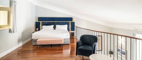 A bedroom with a large bed, a chair, a small table, and a balcony railing.