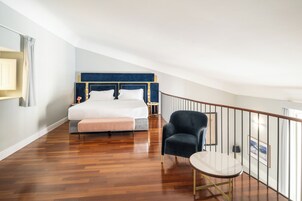 A bedroom with a large bed, a chair, a small table, and a balcony railing.