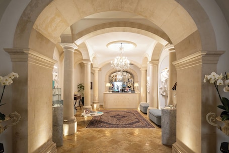 A grand lobby with arched ceilings, marble columns, a chandelier, and a reception desk.