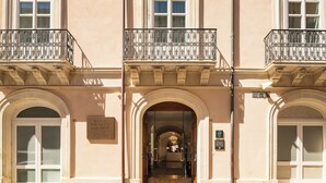 Un edificio con tres balcones, una entrada central con arco y un cartel que indica que es un pequeño hotel de lujo.