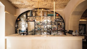 Un bar con techo de piedra, encimera de mármol y estanterías llenas de botellas de licores.
