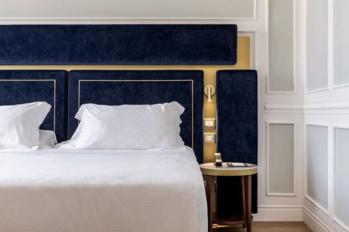 Habitación de hotel con una cama grande, una mesita de noche y una lámpara fijada a la pared.