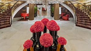 A grand lobby with a large chandelier, red flowers in vases, and a staircase. - The Claridges, New Delhi (New Delhi)