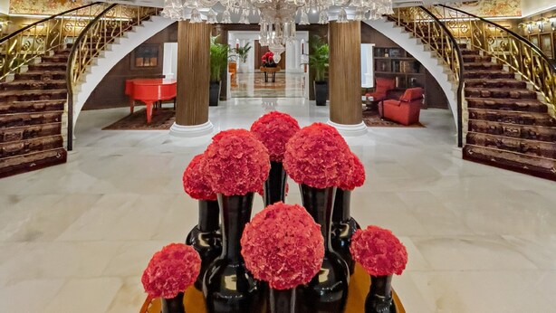 A grand lobby with a large chandelier, red flowers in vases, and a staircase. - The Claridges, New Delhi (New Delhi)