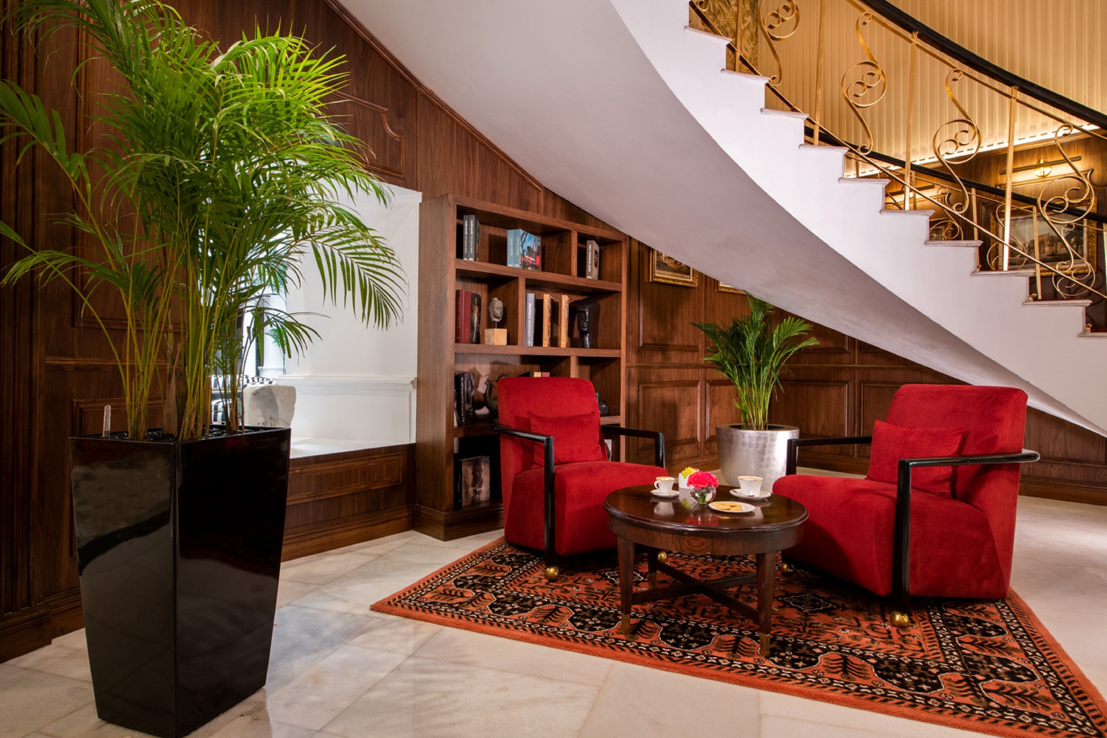 A spacious living area with a large potted plant, a red armchair, a coffee table, and a bookshelf.