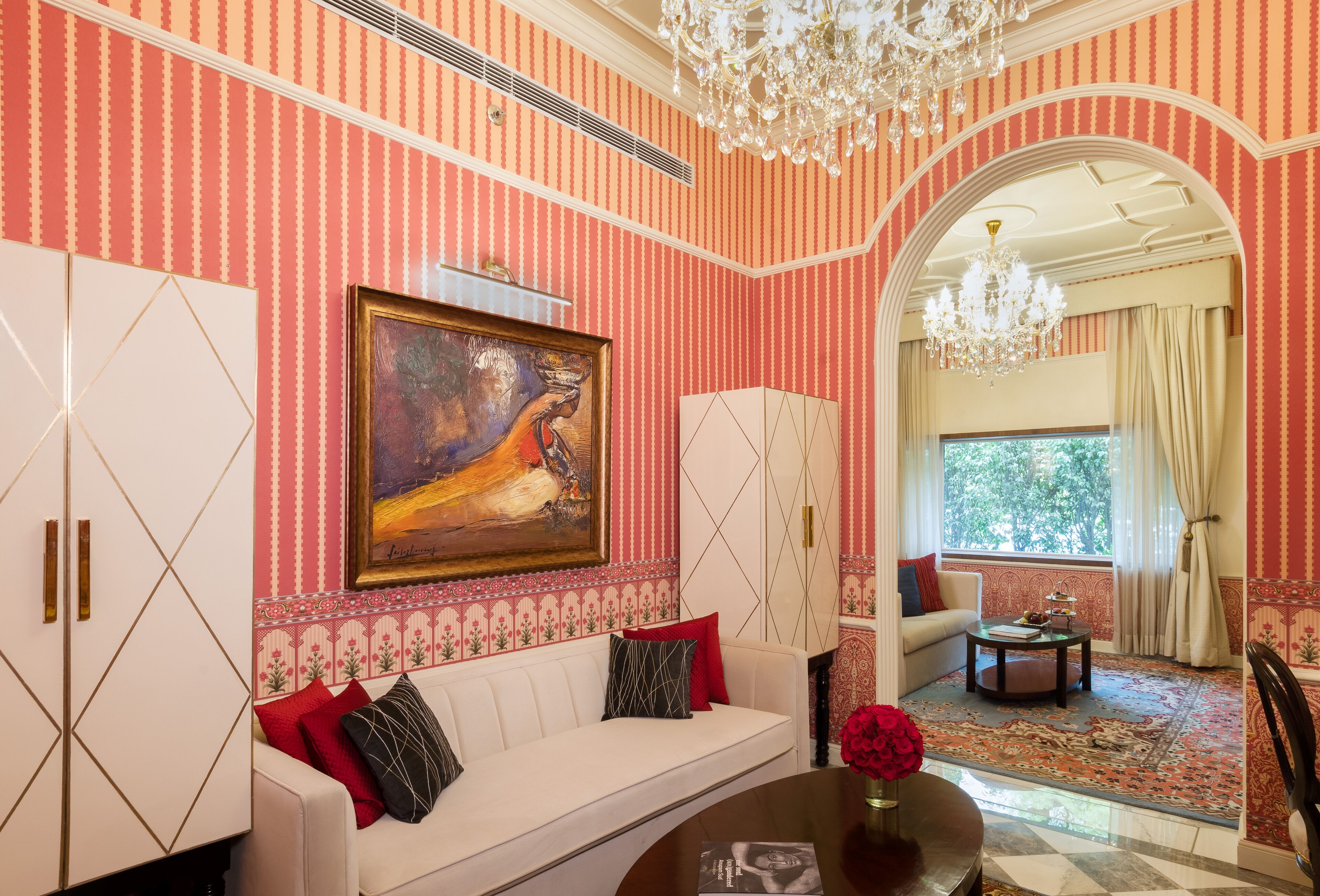 A living room with a white sofa, a painting, a chandelier, and a view through an archway.