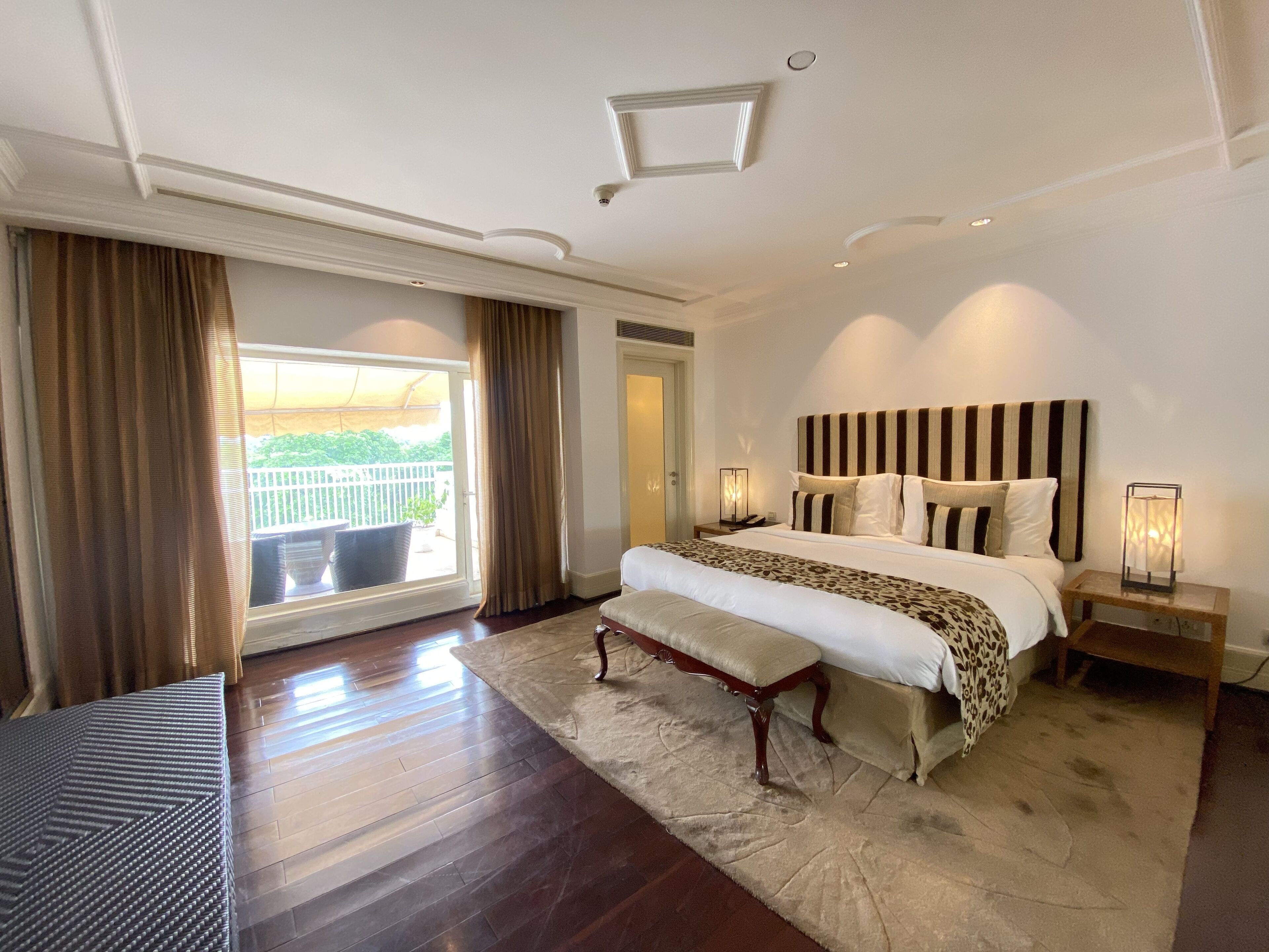 A spacious bedroom with a large bed, a wooden floor, a balcony view, and a modern ceiling design.