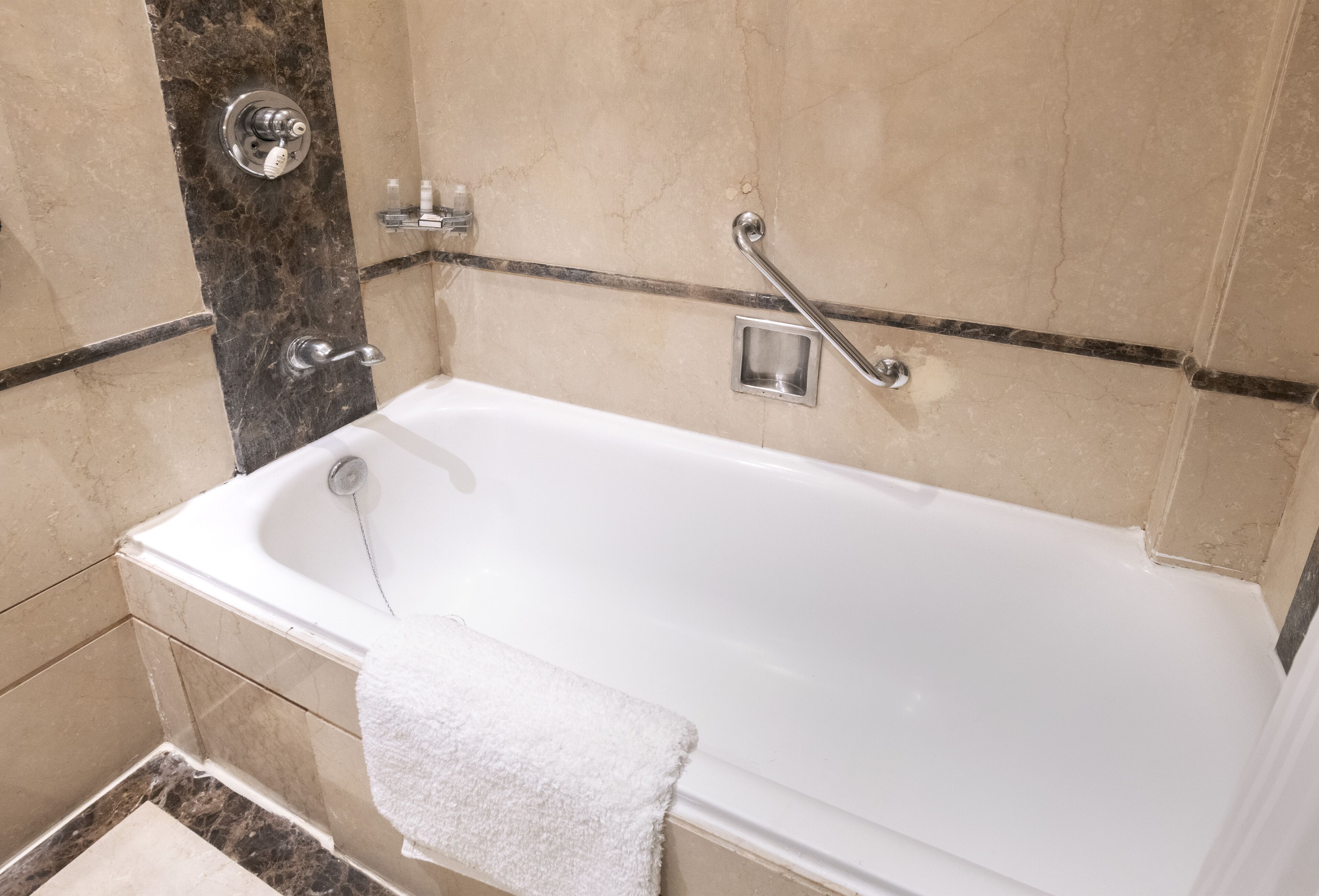 A bathroom with a white bathtub, a grab bar, a towel, and a showerhead.