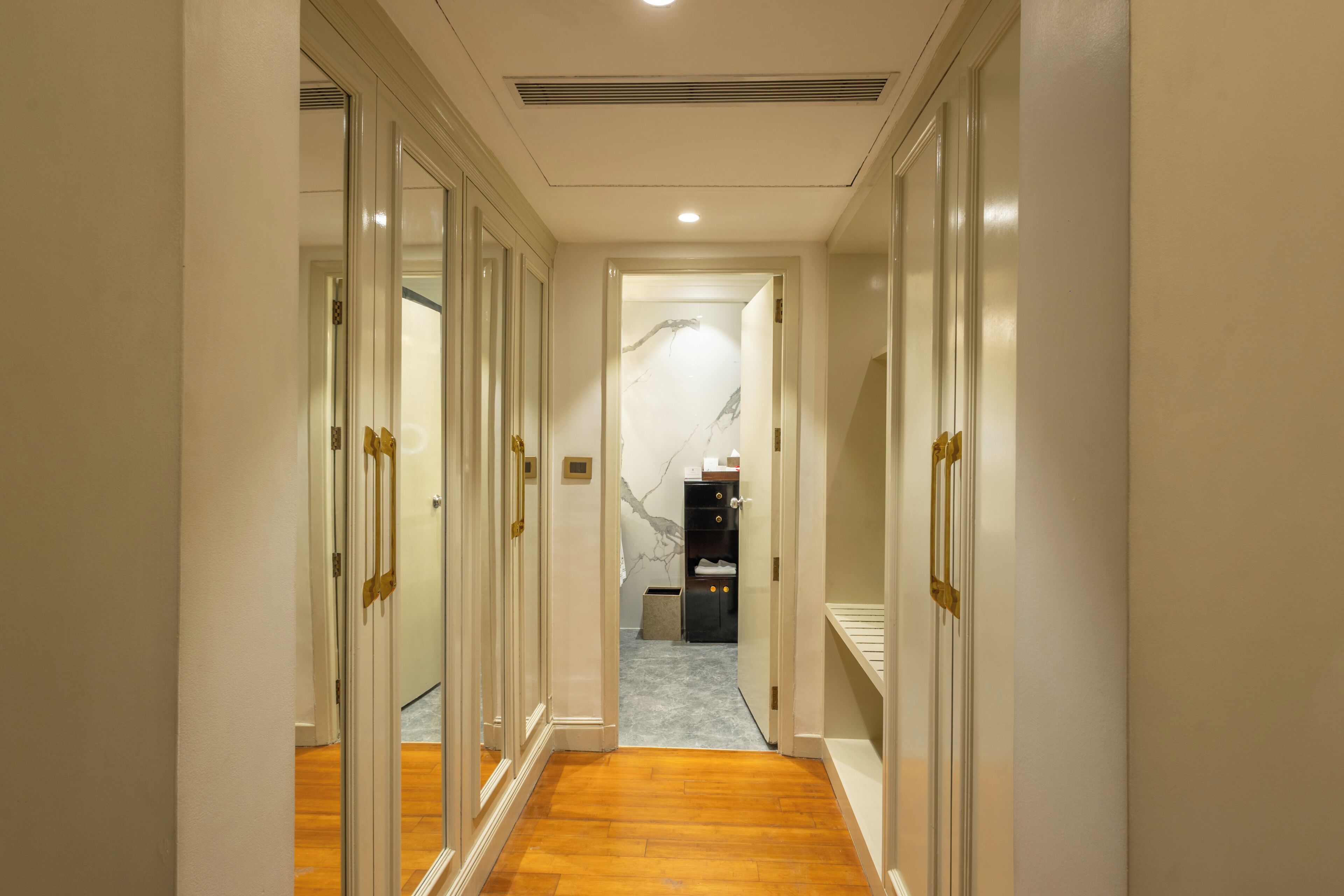 Un passadís amb una paret de marbre, terra de fusta i una porta que condueix a una habitació amb un llit.
