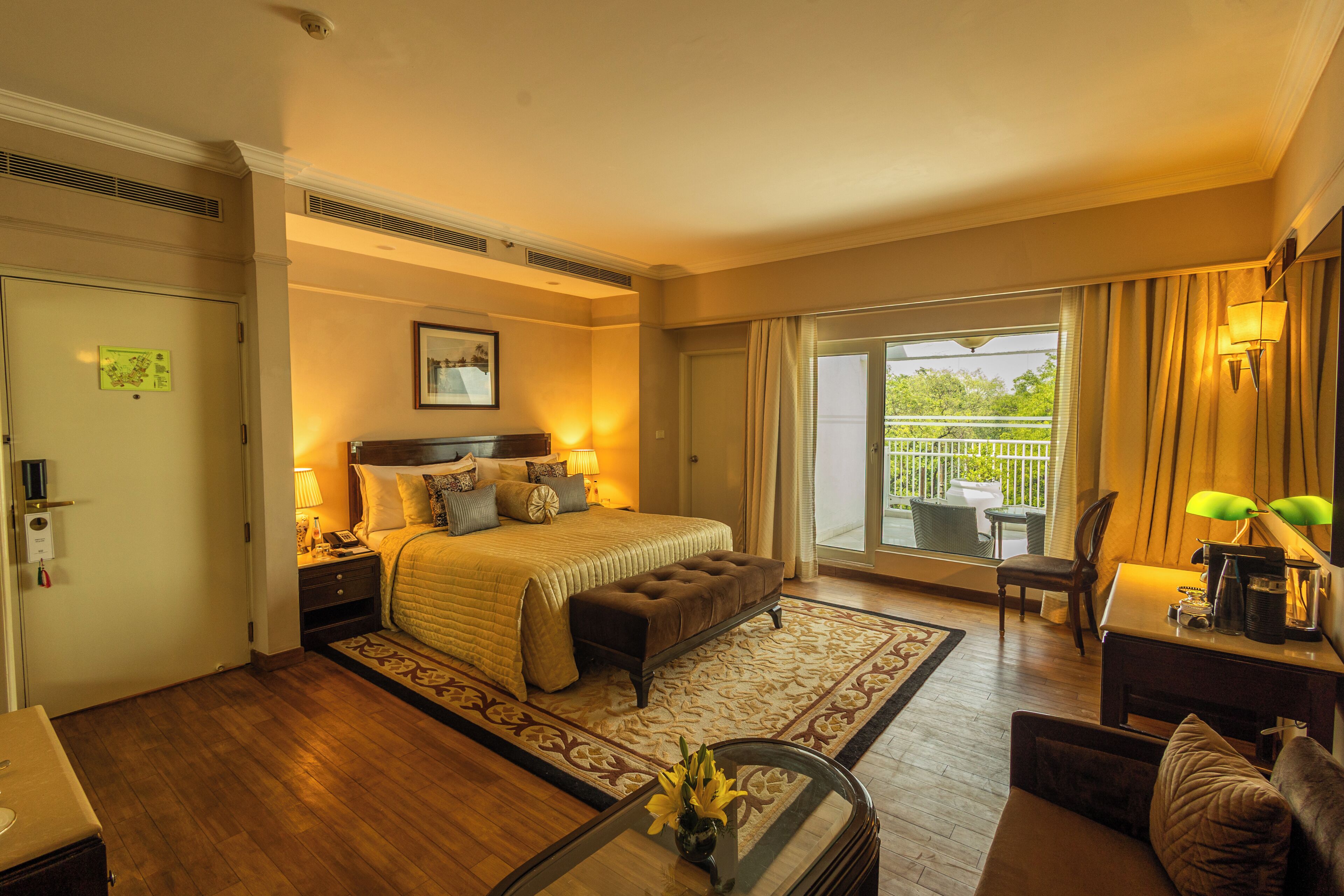 A hotel room with a large bed, a desk with a chair, a balcony with a view, and a door with a keycard lock.