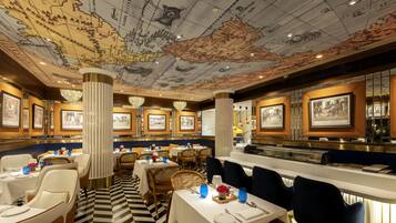Un restaurant dont le plafond est décoré de cartes, avec des tables blanches et des chaises bleues.