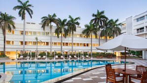 A hotel pool area with a checkered floor, lounge chairs, and umbrellas. - The Claridges, New Delhi (New Delhi)