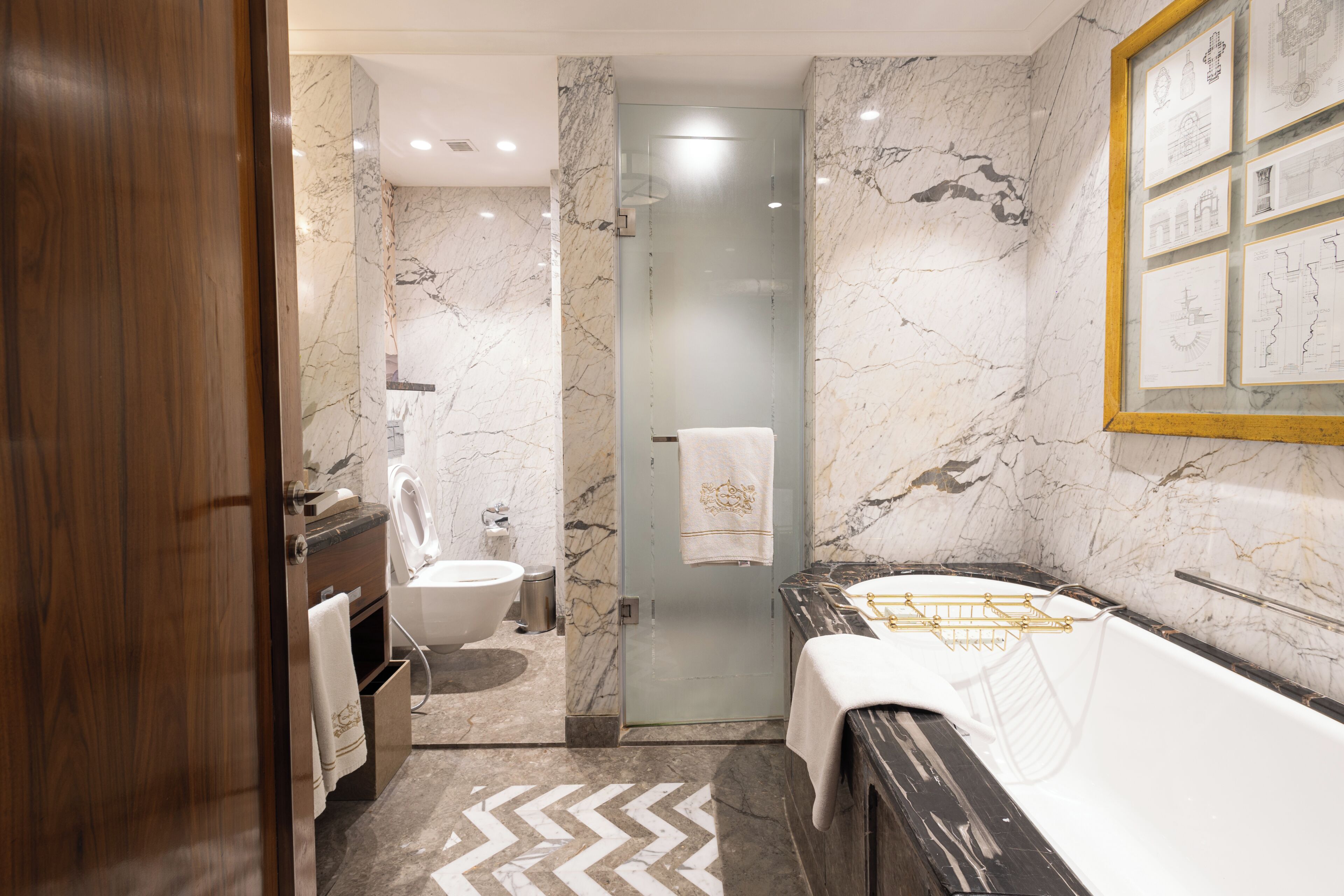 Une salle de bain moderne avec un mur en marbre, une douche en verre, un meuble-lavabo en bois et une baignoire dotée de robinetterie dorée.