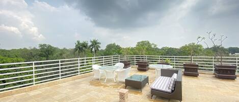 A rooftop terrace with outdoor furniture, a railing, and a view of greenery and trees.