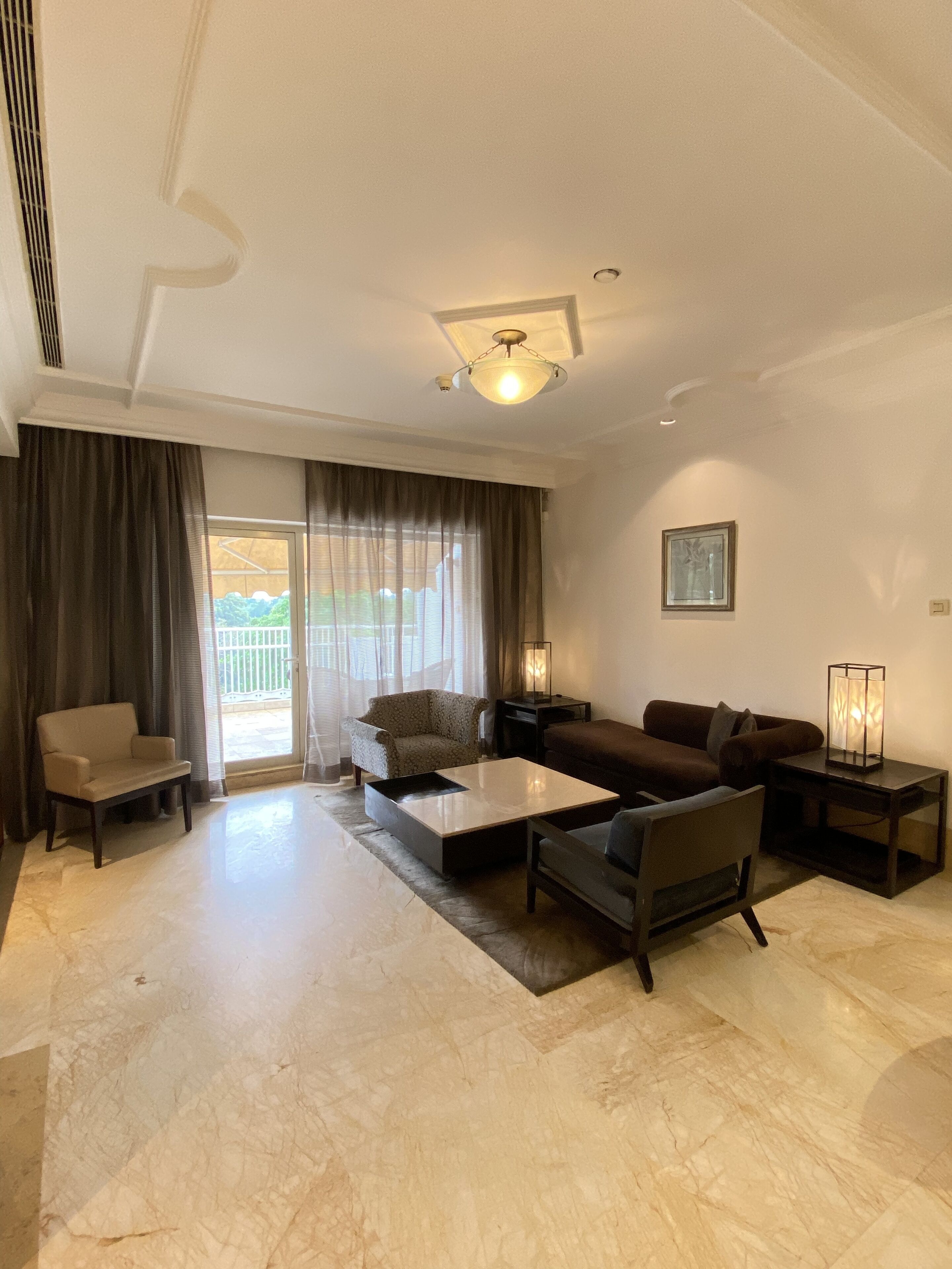 A spacious living room with a large window, a sofa set, a coffee table, and a lamp.