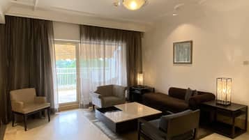 A spacious living room with a large window, a sofa set, a coffee table, and a lamp.