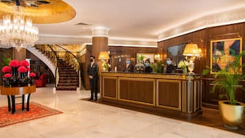 Un vestíbulo con una imponente escalera, una recepción y un candelabro.