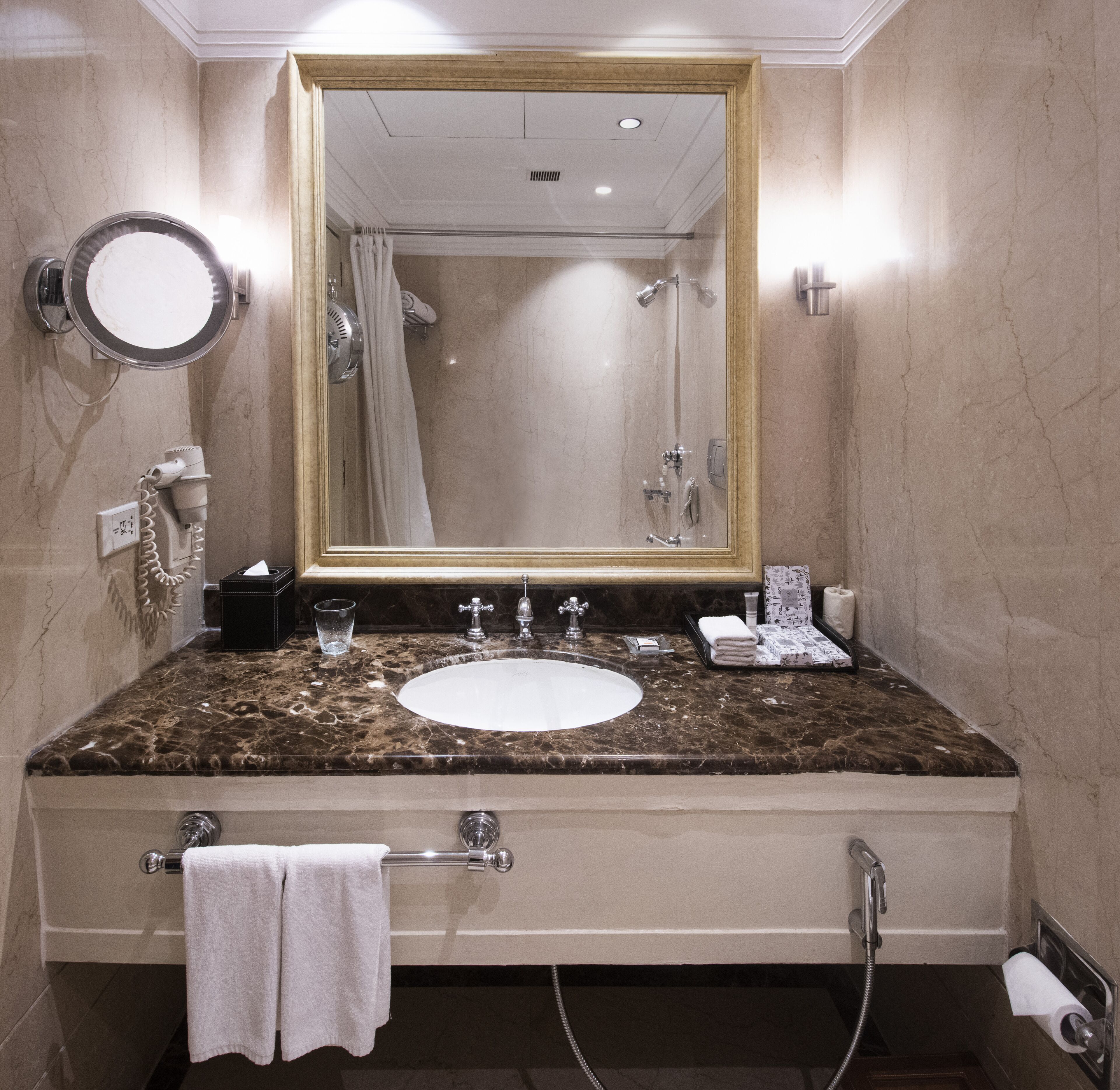 A bathroom with a marble sink, a large mirror, a hairdryer, a towel rack, and a shower.