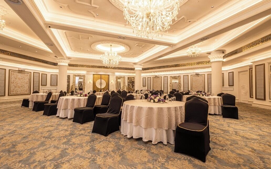 Un salón de banquetes con mesas redondas, sillas negras, candelabros y detalles ornamentales en el techo.