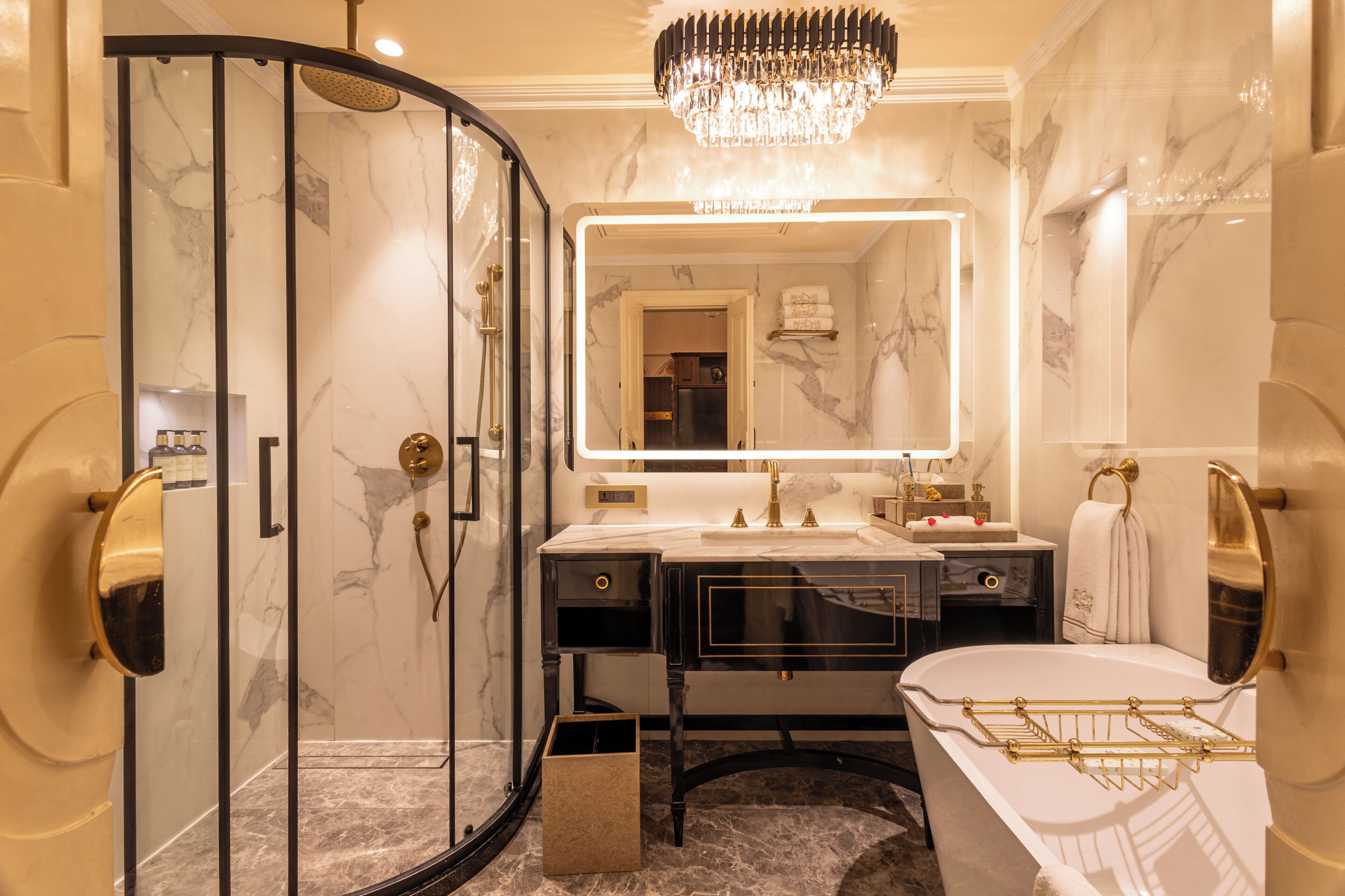 A luxurious bathroom with a glass-enclosed shower, a marble vanity, and a large mirror with a gold frame.