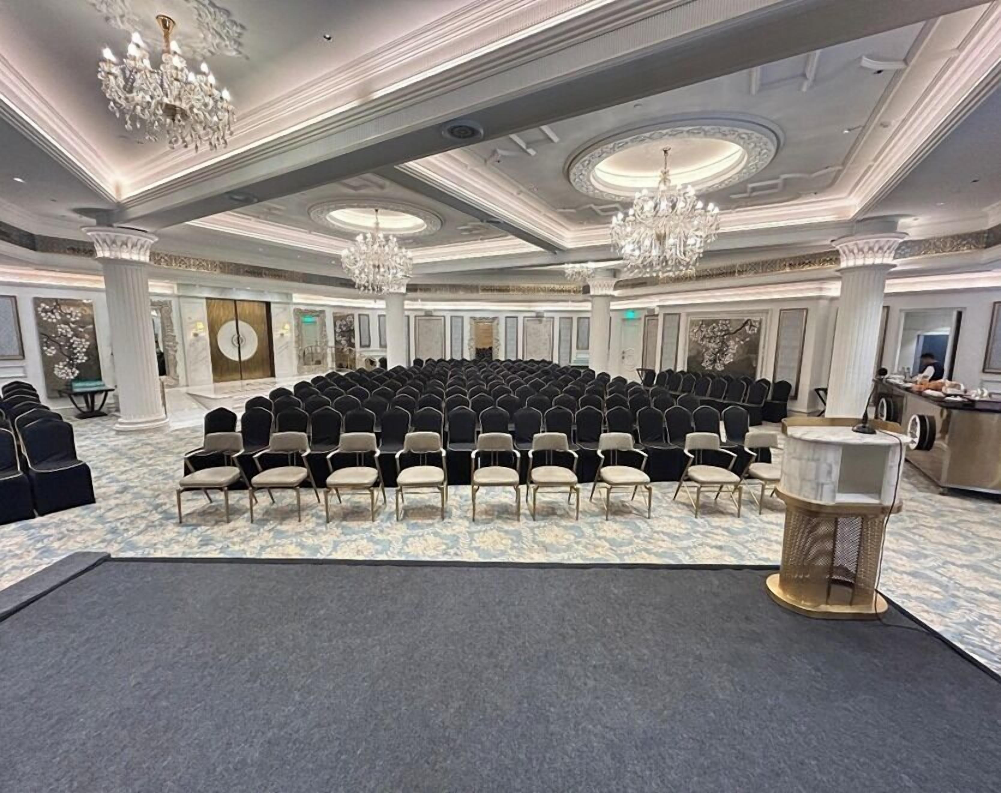 Un salón de conferencias con filas de sillas, un escenario y una zona de bar.