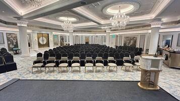 Un salón de conferencias con filas de sillas, un escenario y una zona de bar.