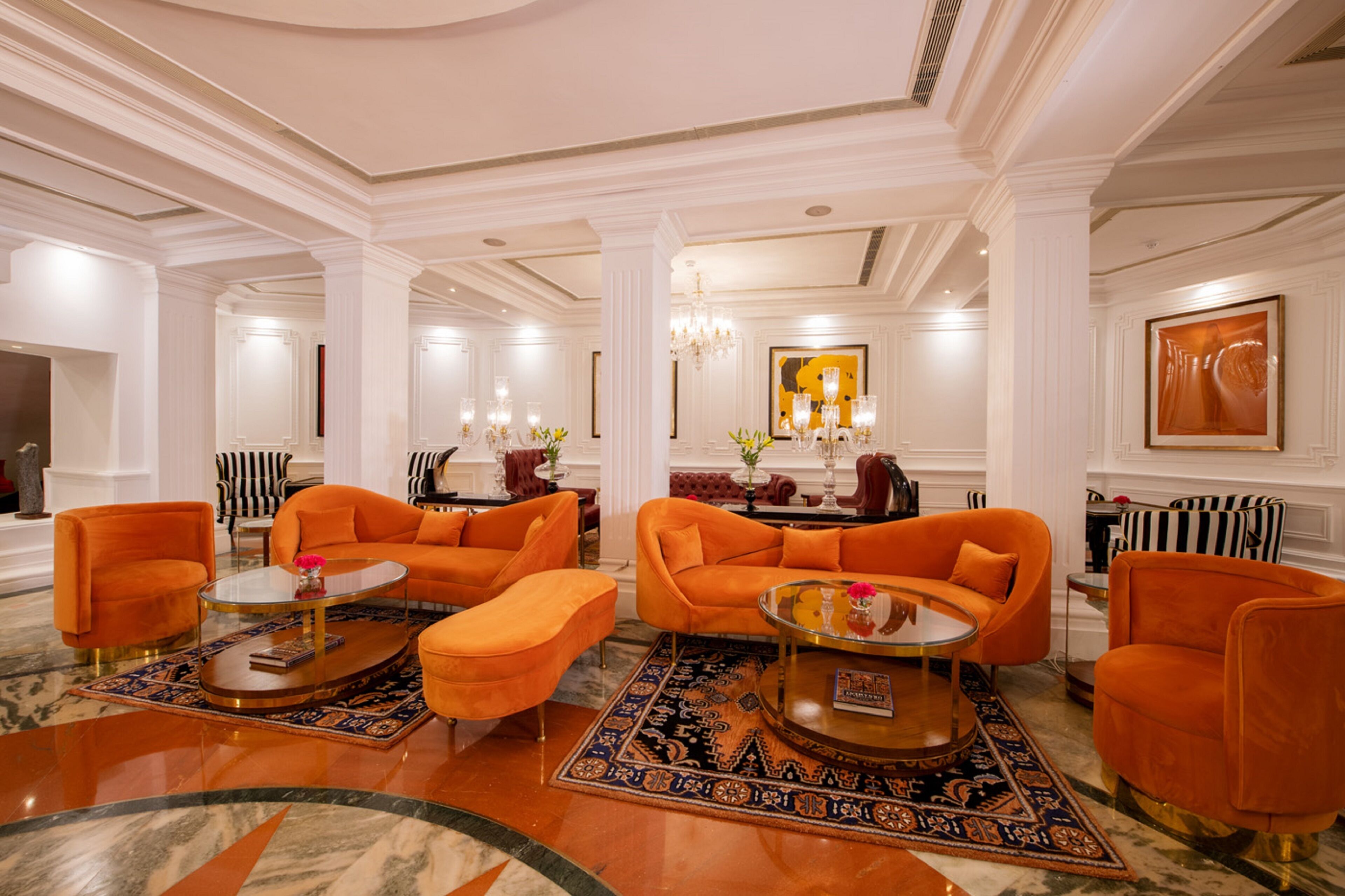 A spacious lobby with a modern orange sofa set, a glass coffee table, and a patterned rug.