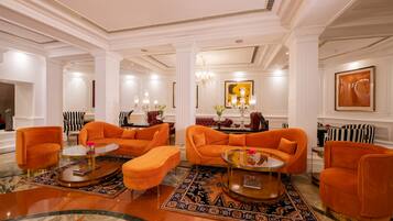 A spacious lobby with a modern orange sofa set, a glass coffee table, and a patterned rug.